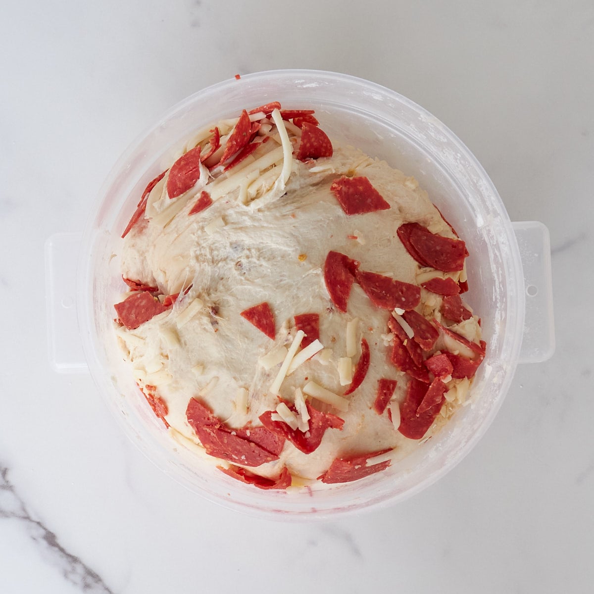 Chopped pepperonis and shredded mozzarella cheese in sourdough bread dough in a 2-quart container.