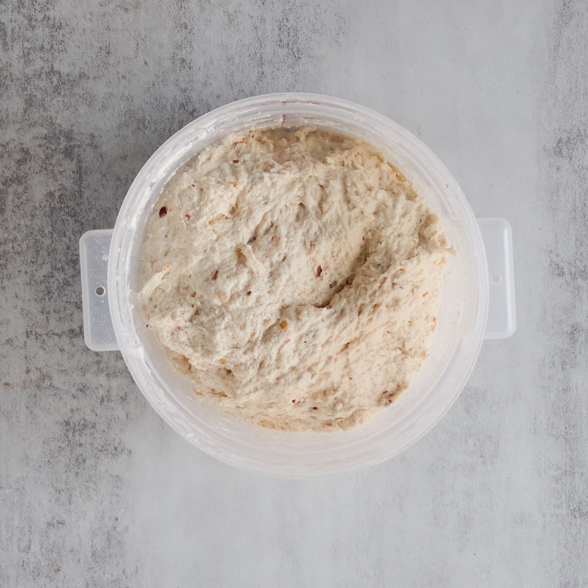 Sourdough bread dough mixed in a plastic 2-quart container on a gray counter.