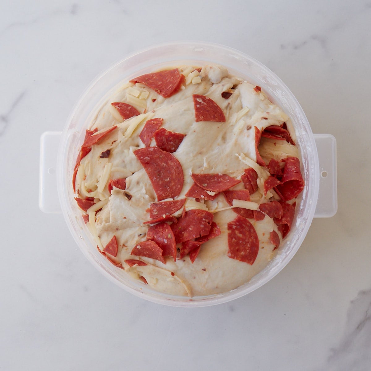 Chopped pepperonis and shredded mozzarella cheese in sourdough bread dough in a 2-quart container after the first rise.