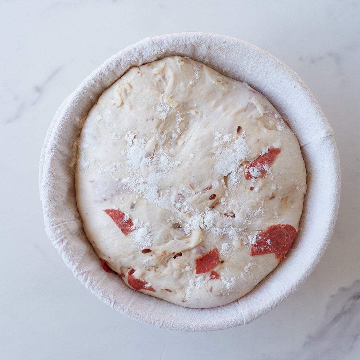 Pepperoni sourdough bread in a round banneton basket on a marble counter after the second rise.