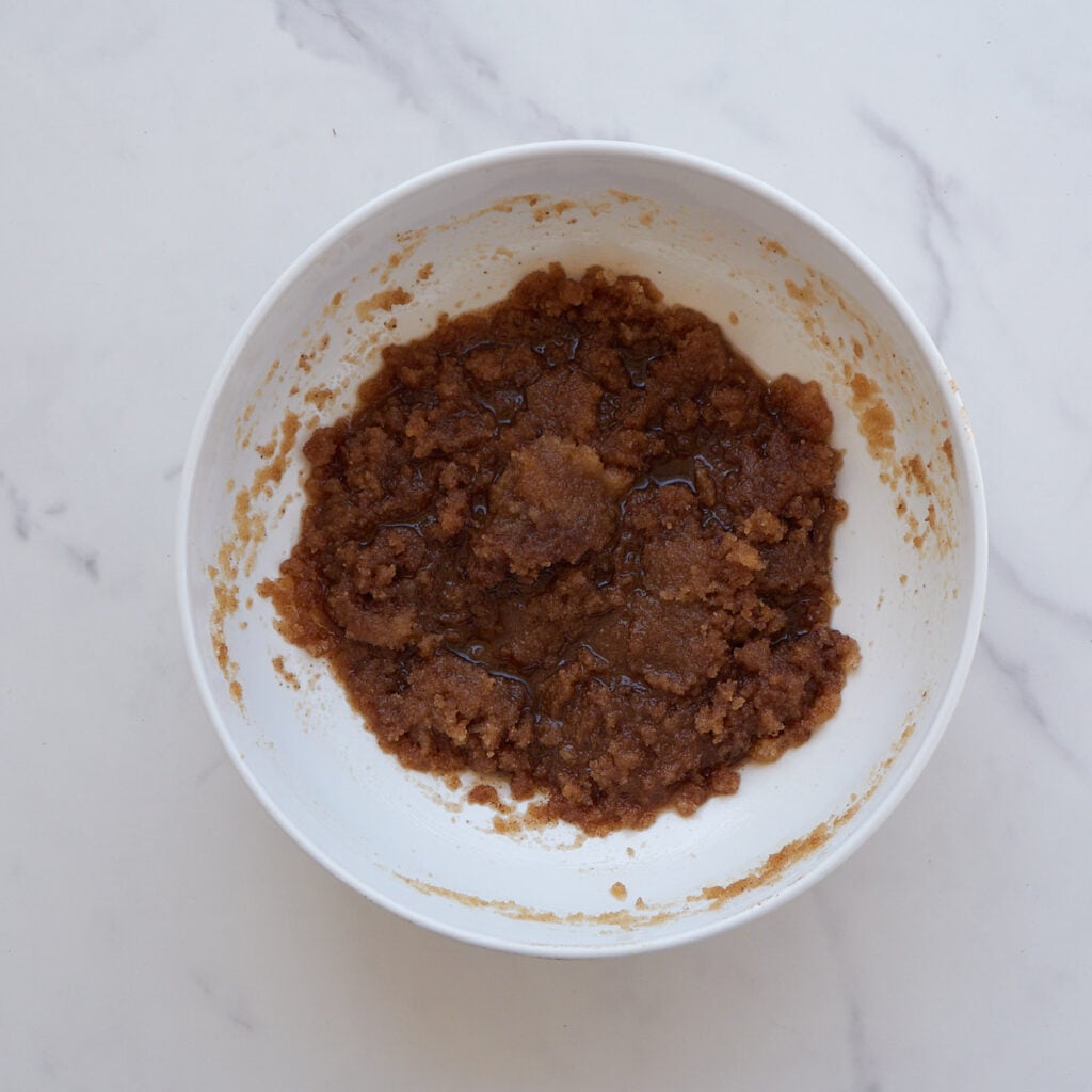 Wet ingredients added to brown butter and sugar in a white bowl.