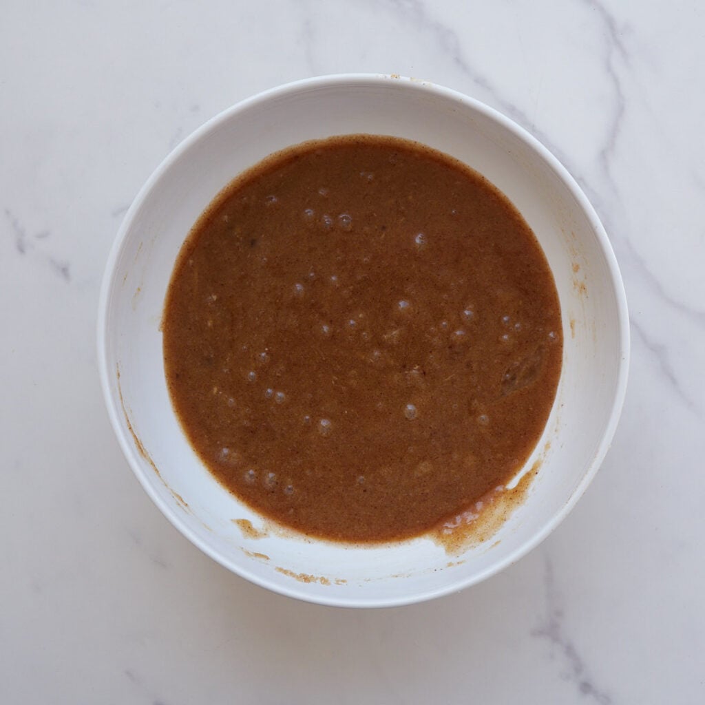 Brown sugar and white sugar added to brown butter in a white bowl.