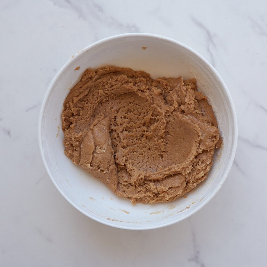 Dry ingredients added to wet ingredients in a white bowl for cadbury egg sourdough cookie bars.