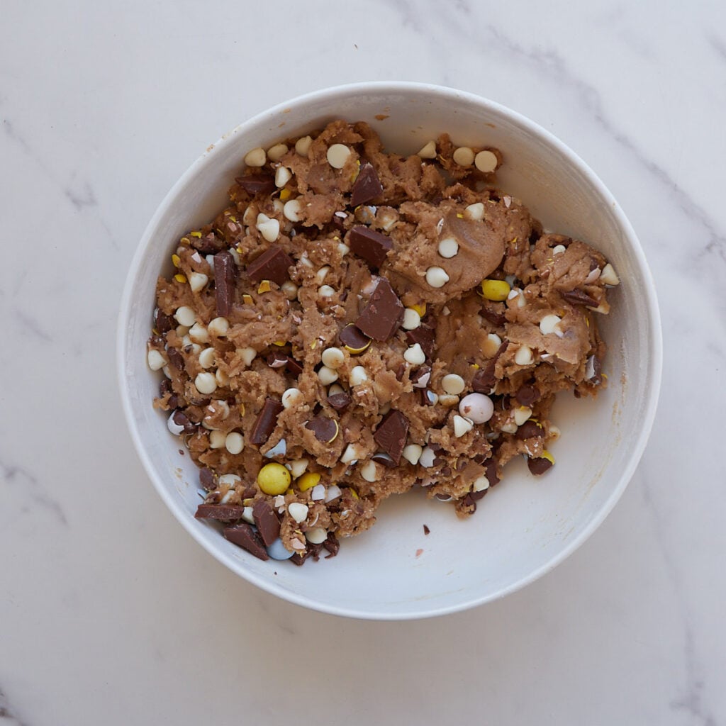 Chocolate and cadbury eggs added to cookie dough in a white bowl.