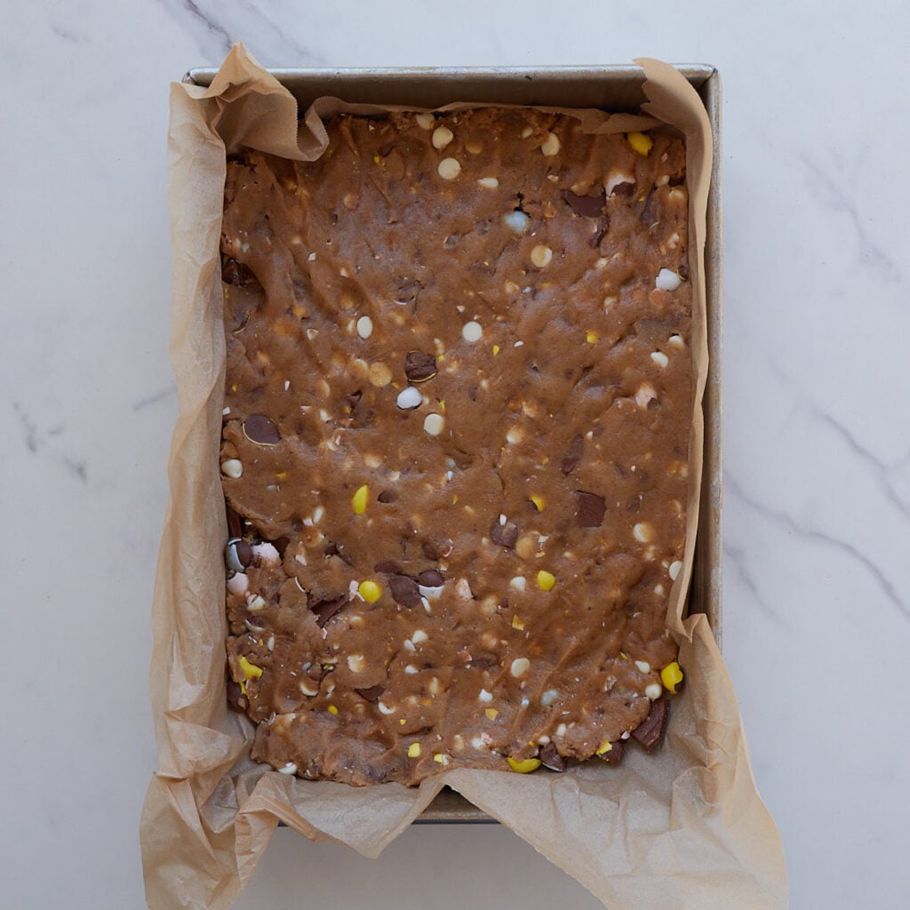 Cookie dough for Cadbury egg sourdough cookie bars pressed into a 9x13 pan lined with parchment paper.
