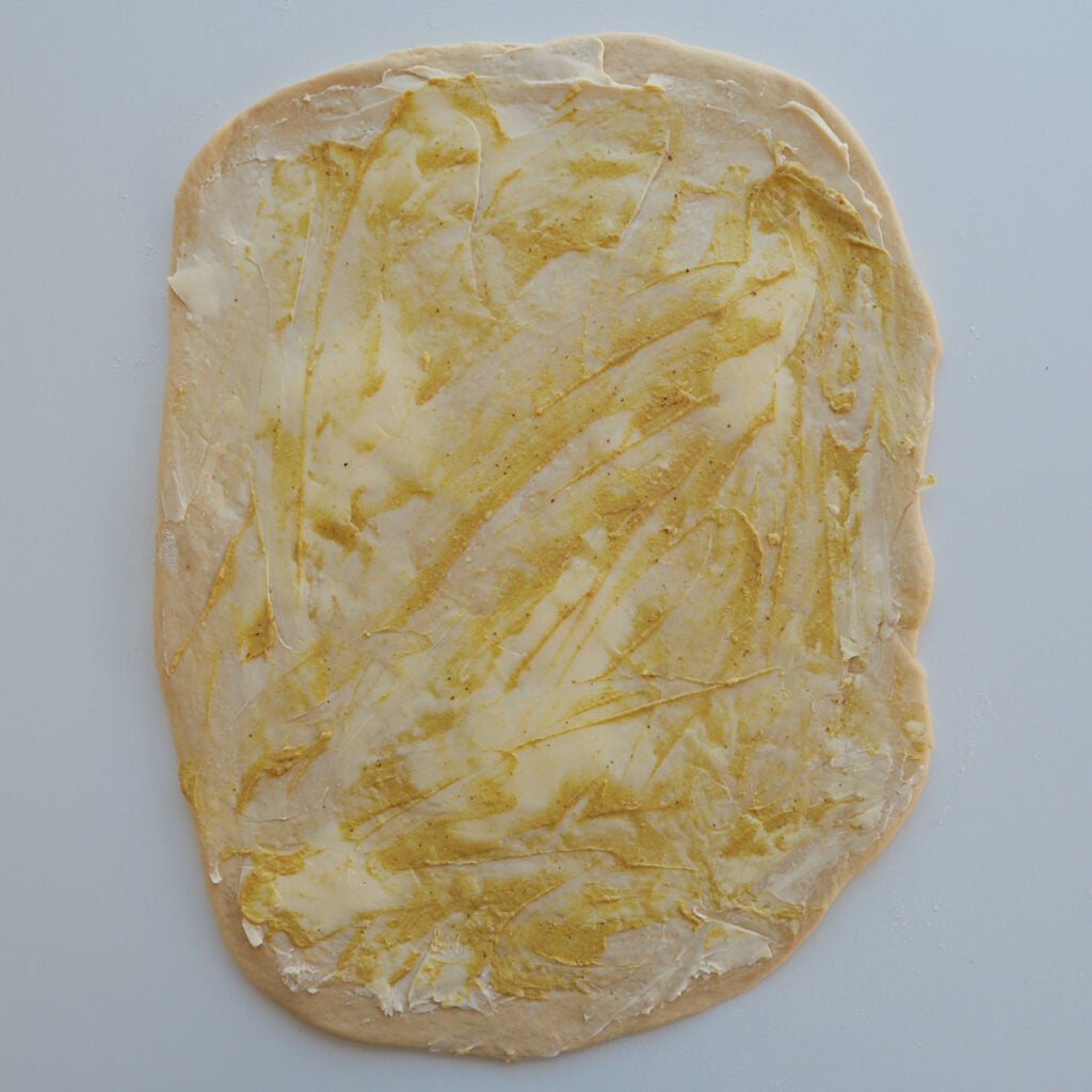 Dough for Sourdough Ham and Cheese Rolls rolled out into a rectange with djion mustard and butter spread over the top.