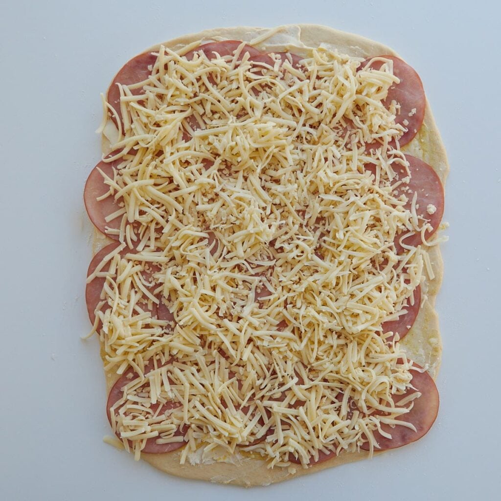 Dough for Sourdough Ham and Cheese Rolls rolled into a rectangle with ham and cheese added on top.