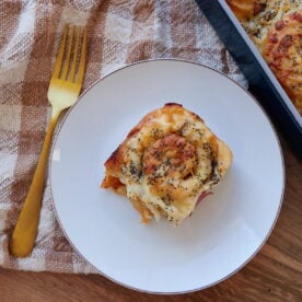 One Sourdough Ham and Cheese Roll on a white plate with a gold fork next to it.