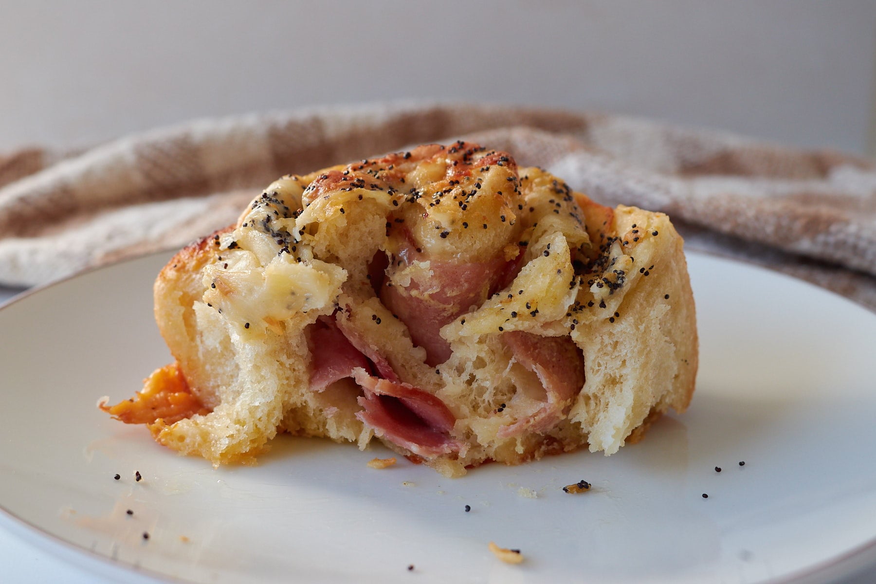 A bite taken out of a Sourdough Ham and Cheese Roll on a white plate.