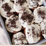 Cookies and Cream Sourdough Chocolate Rolls in a 9x13 pan with cream cheese frosting and crushed oreos on top next to a brown and white cloth napkin.