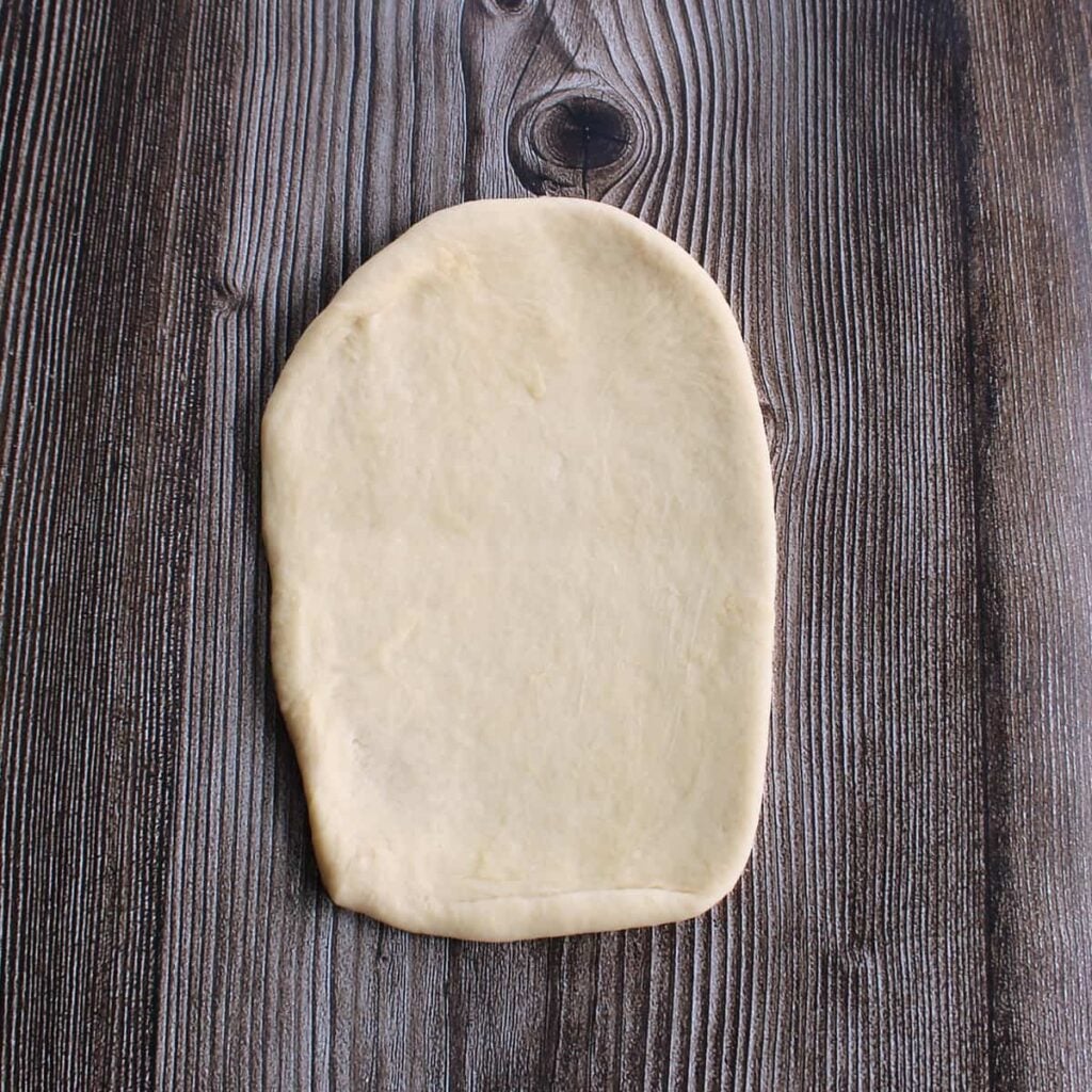 Dough for sourdough discard hot dog buns rolled out into a 6x3 inch rectangle for shaping.