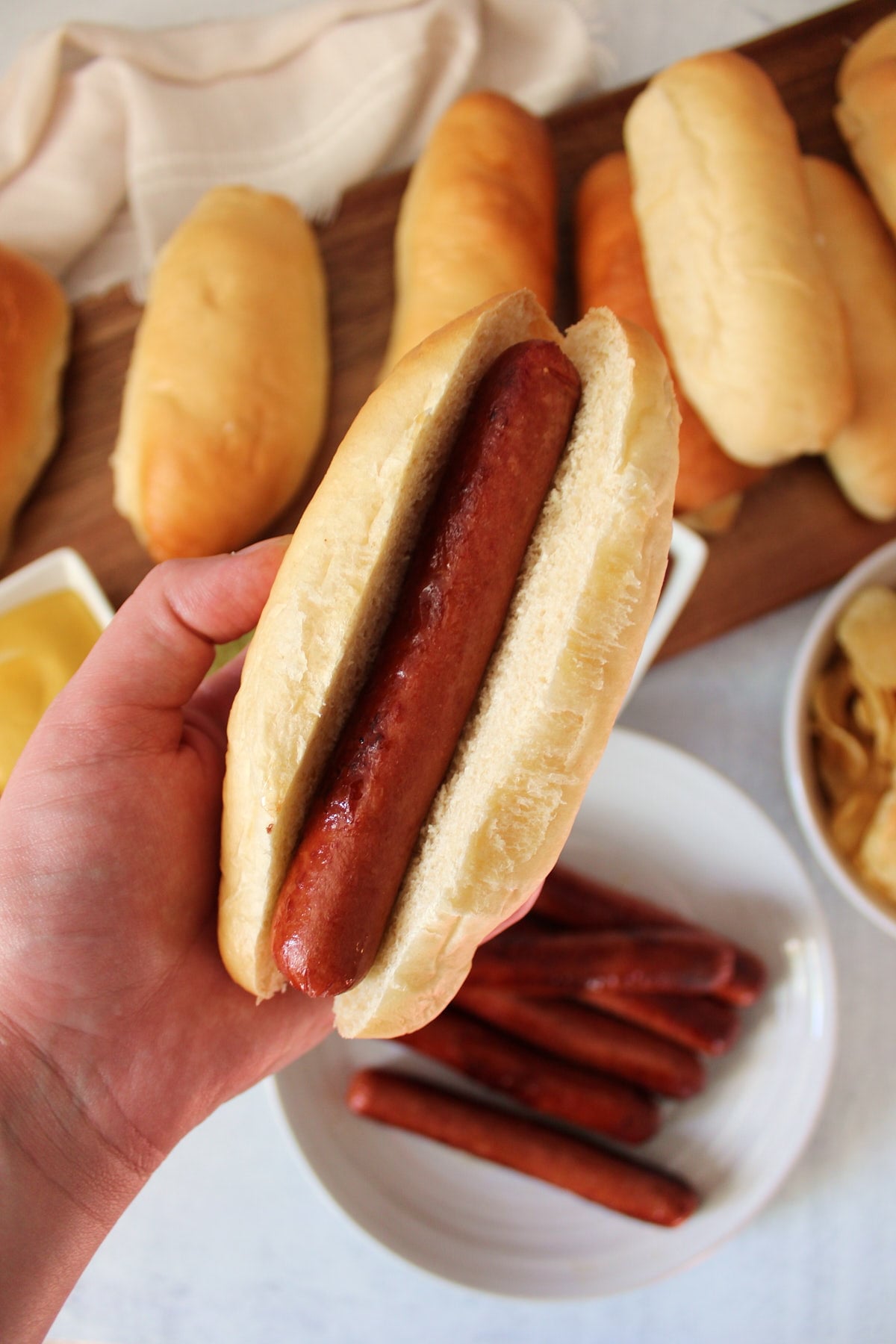 A hand holding a sourdough discard hot dog bun with a hot dog inside.