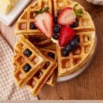 Sourdough waffles on a white plate with blueberries and strawberries on top and one section of the waffle broken off.