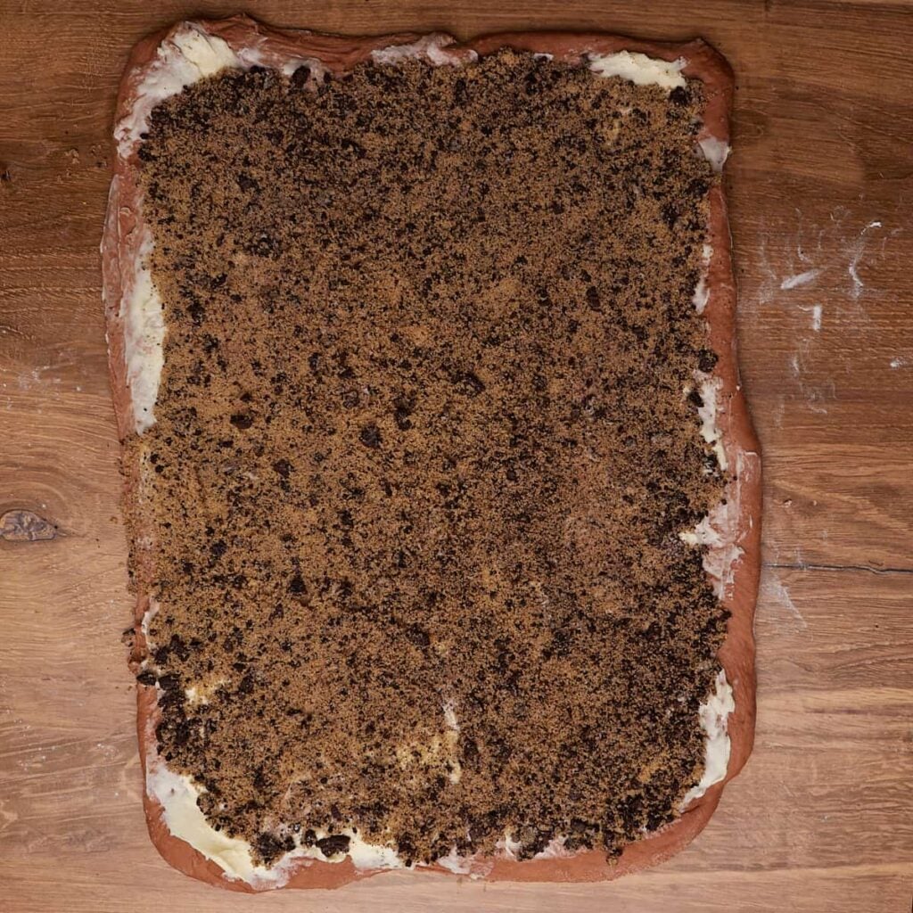 Dough for Cookies and Cream Sourdough Chocolate Rolls rolled out into a rectangle with butter spread over it and oreo filling sprinkled on top.