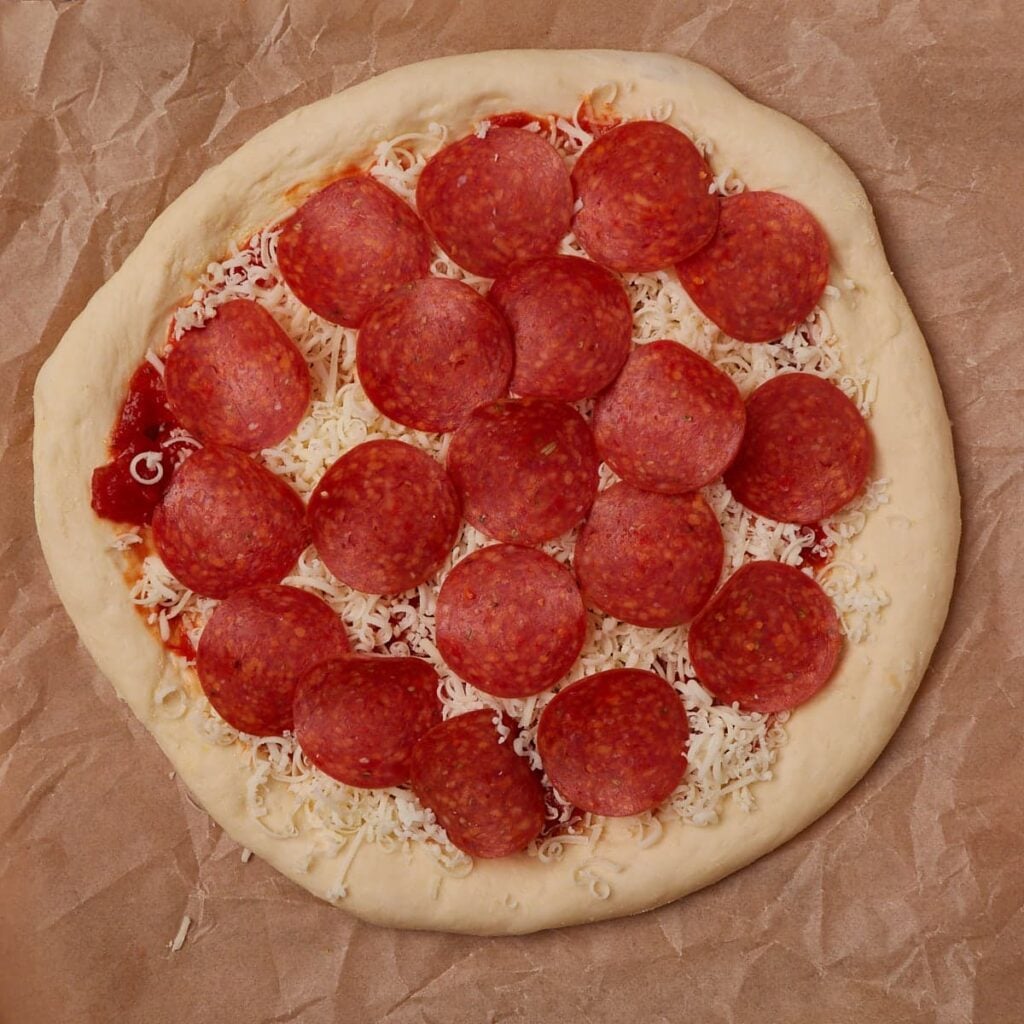 Sourdough discard pizza dough with toppings added on a piece of parchment paper before baking.