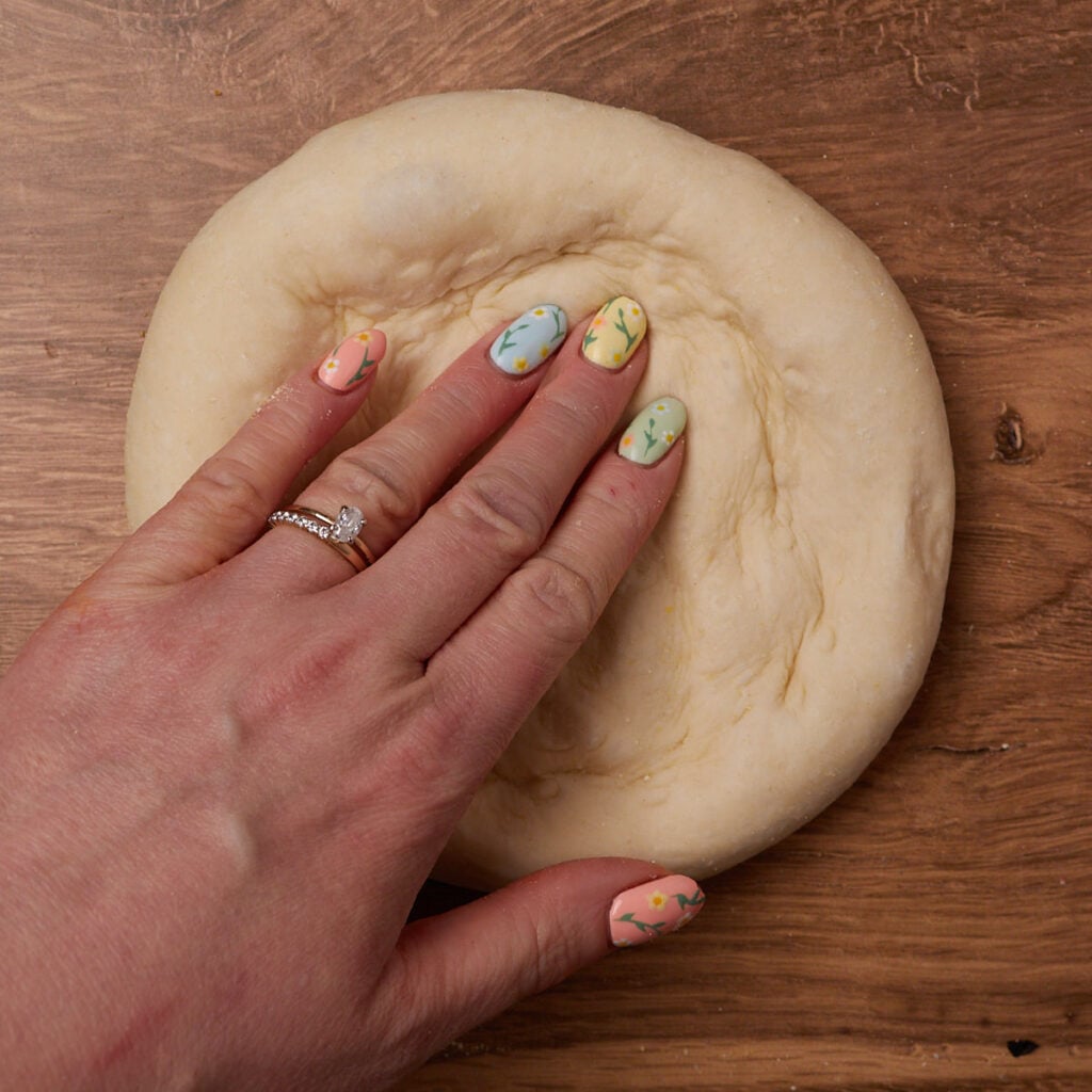 A hand shaping the sourdough discard pizza dough into a 12 inch circle.