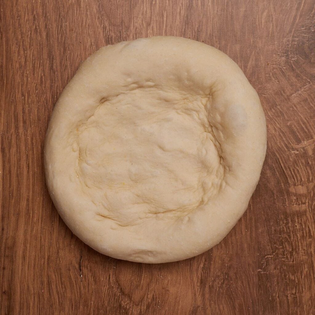 Sourdough discard pizza dough shaped into a 12 inch circle before adding the toppings on a wooden surface.
