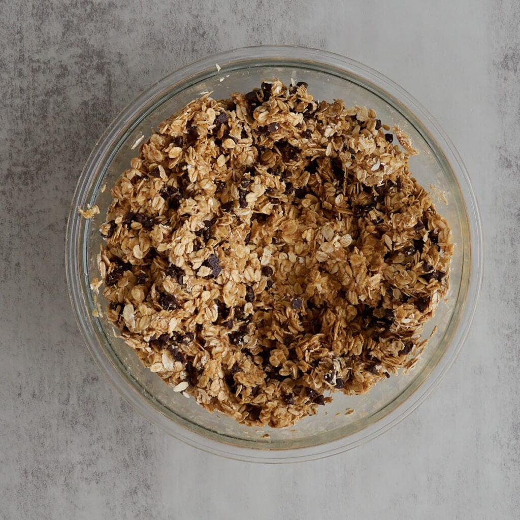 Dry ingredients adds to the wet ingredients for sourdough granola bars in a clear bowl.