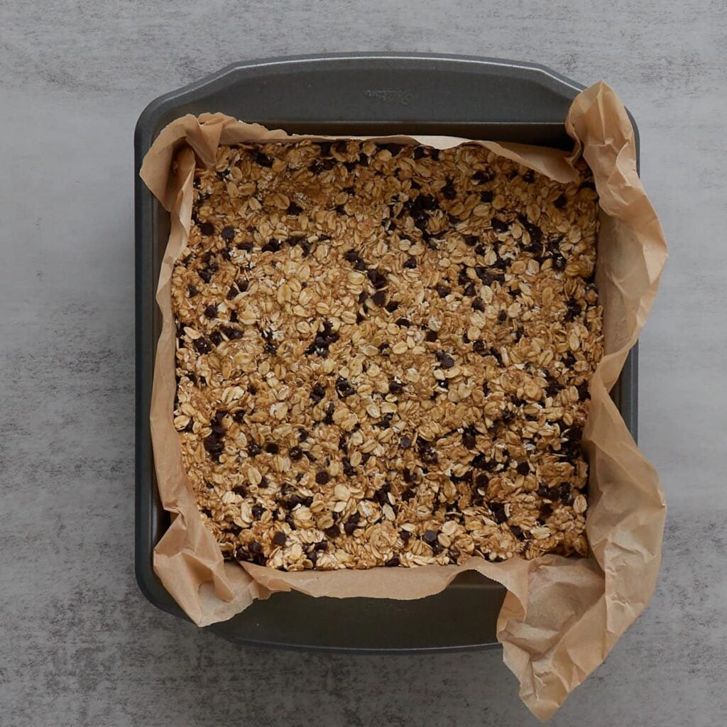 Sourdough granola bars in a 9x9 pan lined with parchment paper before baking.