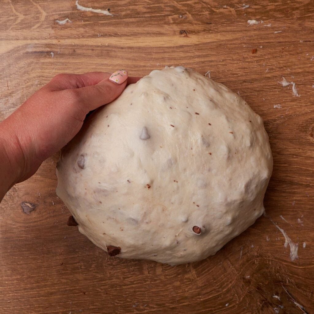 Hand scooping the dough for S'more Sourdough Bread to shape it into a round loaf.