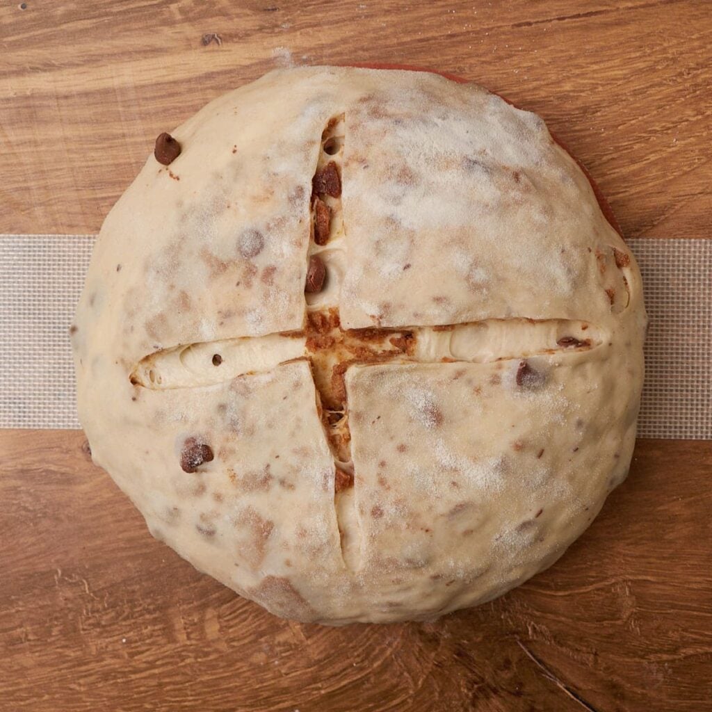 Dough for S'mores Sourdough Bread shaped in a round loaf with an x scored in the center on top of a dough sling.