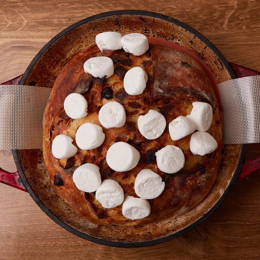 Marshmallows added on top of a freshly baked loaf of S'mores Sourdough Bread before broiling.