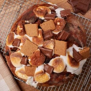 S'mores Sourdough Bread with toasted marshmallows, chocolate squares, and chunks of graham crackers on top on a wire rack.