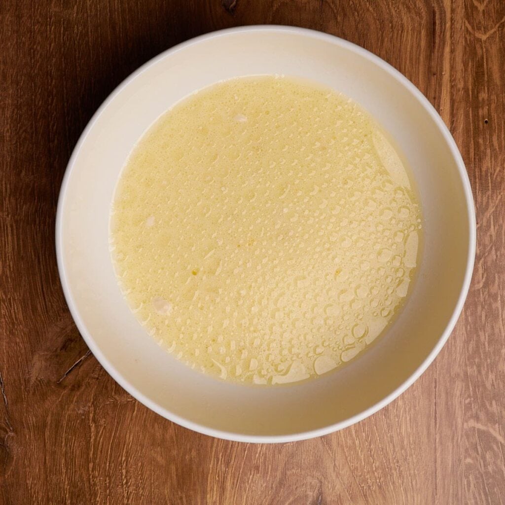Wet ingredients for sourdough waffles mixed together in white bowl.