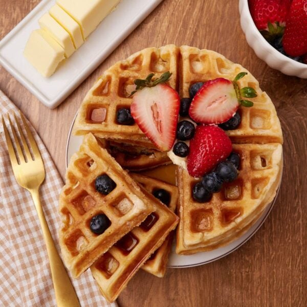 Sourdough waffles on a white plate with blueberries and strawberries on top and one section of the waffle broken off.