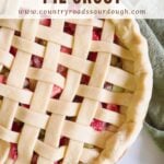 Sourdough pie dough in a lattice top next to a green cloth napkin and with strawberry rhubarb filling.