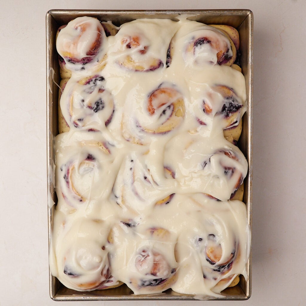 Lemon cream cheese frosting added on top of the Lemon Blueberry Sourdough Rolls in a 9x13 pan.