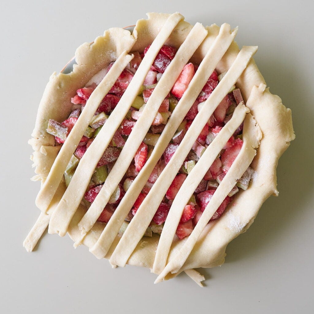 Strip of dough spread across the pie pan to show how to make a lattice crust with sourdough pie dough with strawberry rhubarb filling.
