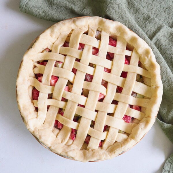 Sourdough pie dough in a lattice top next to a green cloth napkin and with strawberry rhubarb filling.