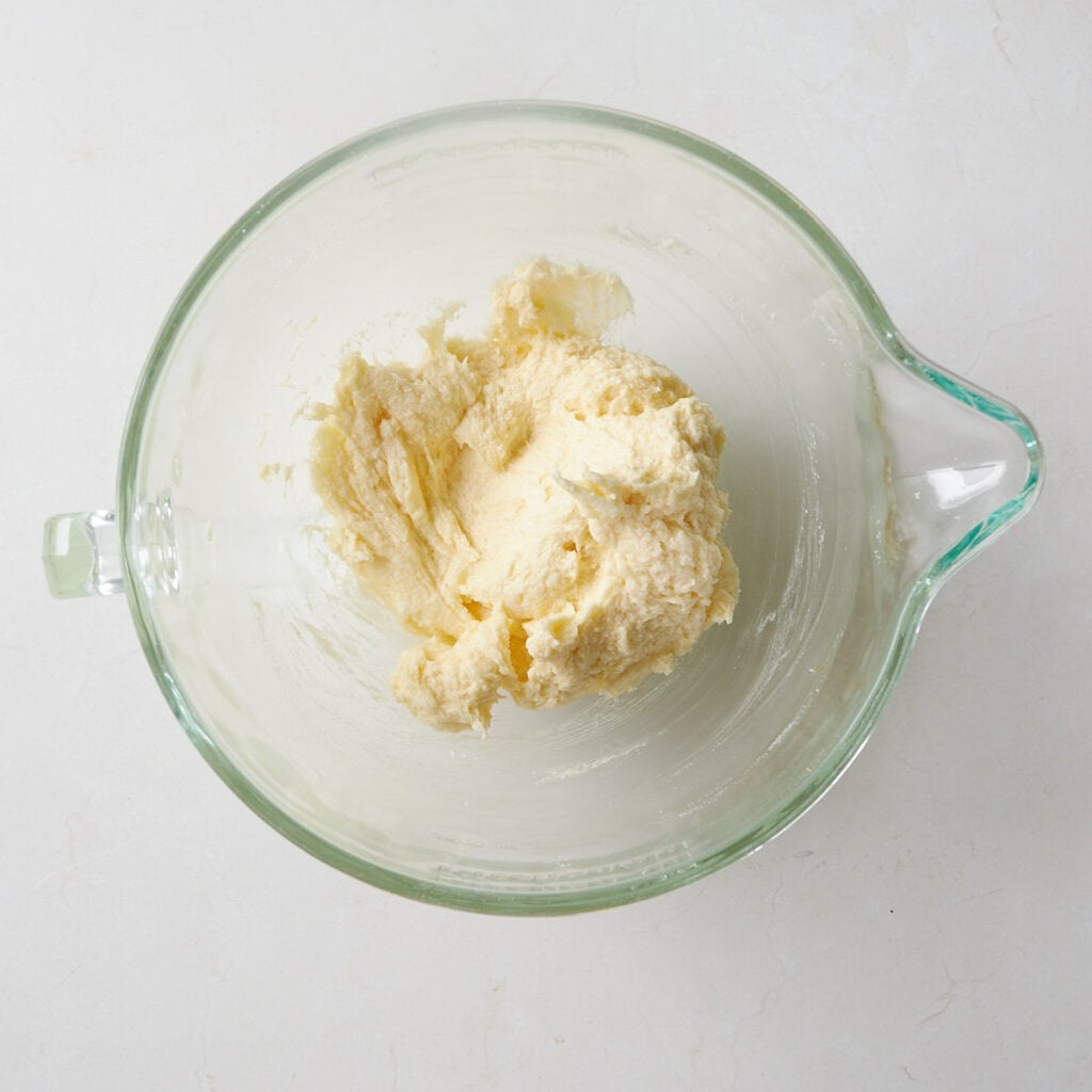 Wet ingredients added to the creamed butter and sugar in a clear mixing bowl for Sourdough Sprinkle Cookies.