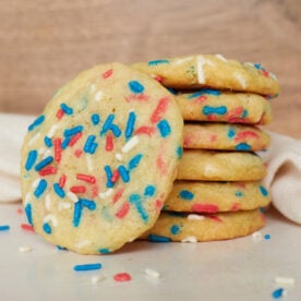 Sourdough Sprinkle Cookies stacked on top of each other with one off to the side next to a white cloth napkin.