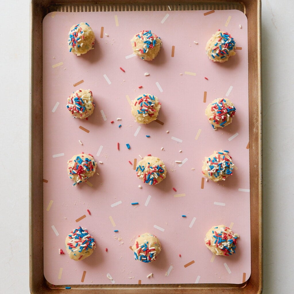 Sourdough Sprinkle Cookie dough balls on a lined baking sheet.