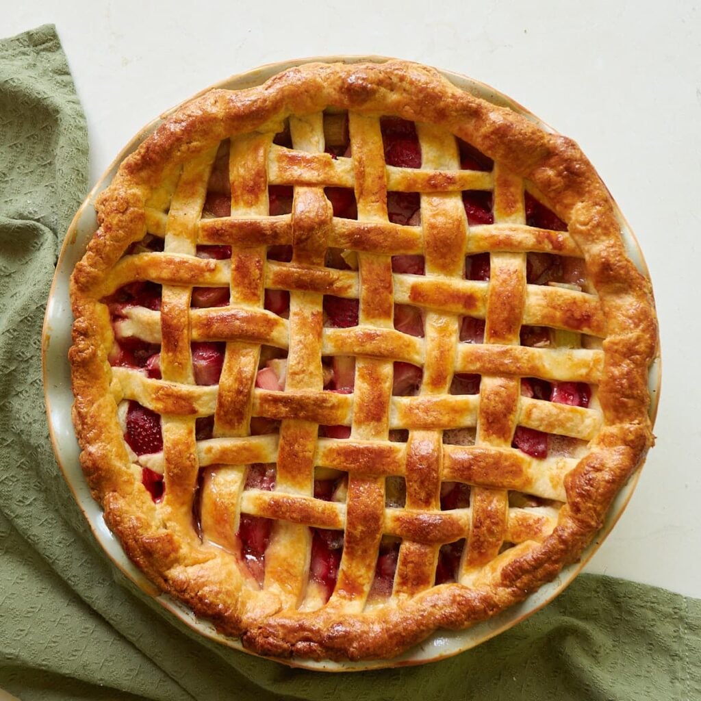 Freshly baked sourdough strawberry rhubarb pie next to a green cloth napkin.