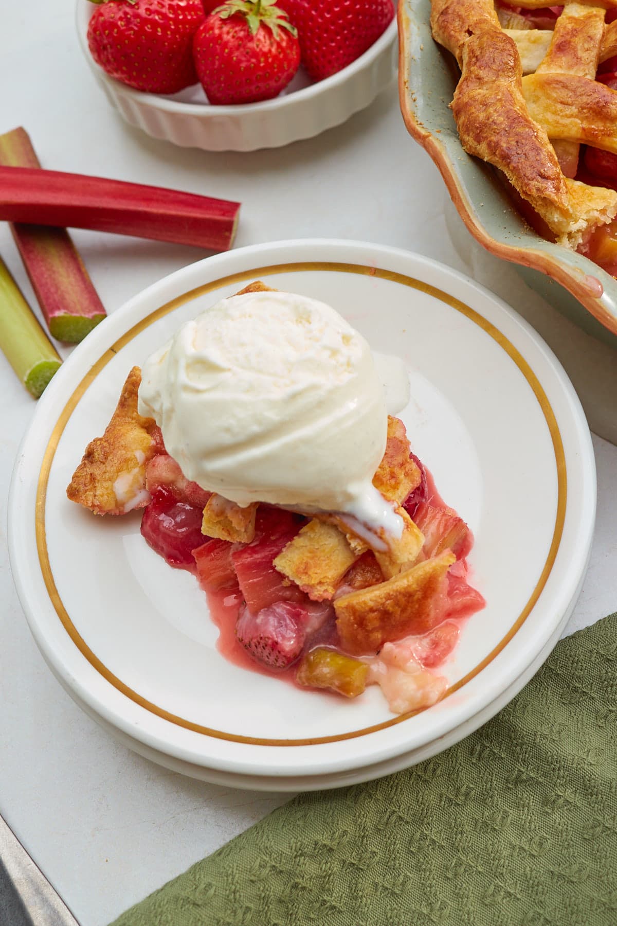 Slice. of straweberry rhubarb pie with a scoop of vanilla ice cream on top. 