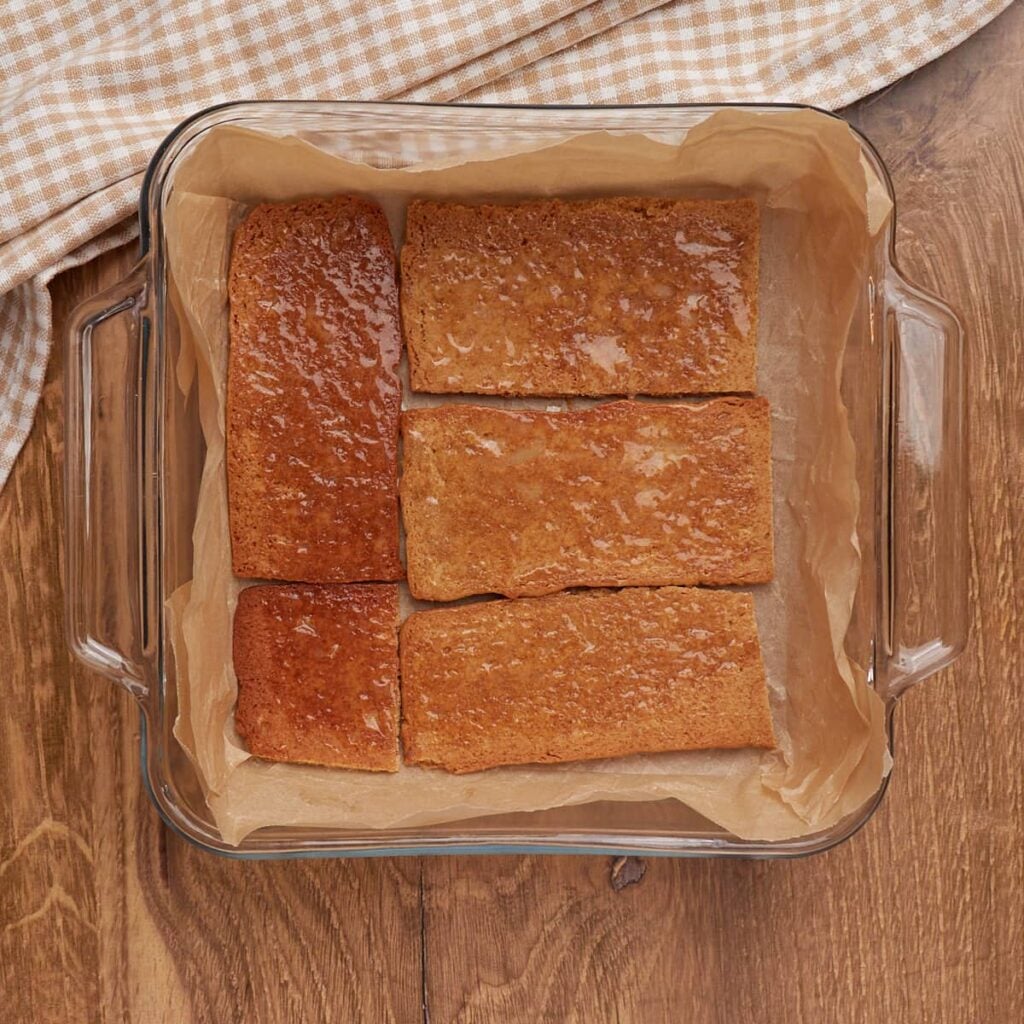 Graham crackers with melted butter layered in the bottom of an 8x8 pan lined with parchment paper for Sourdough S'mores Cookie Bars.