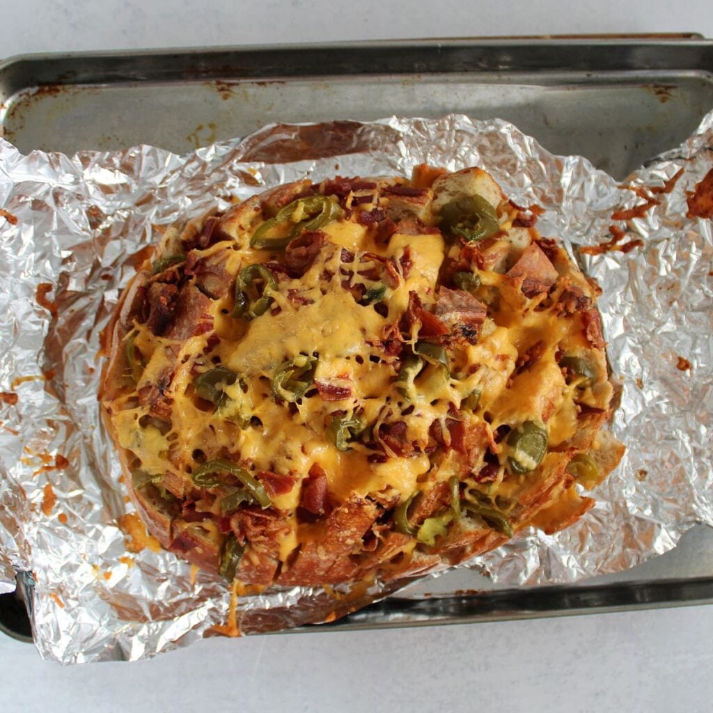 Freshly baked jalapeno cheddar bacon pull apart bread on top of foil on a sheet pan.