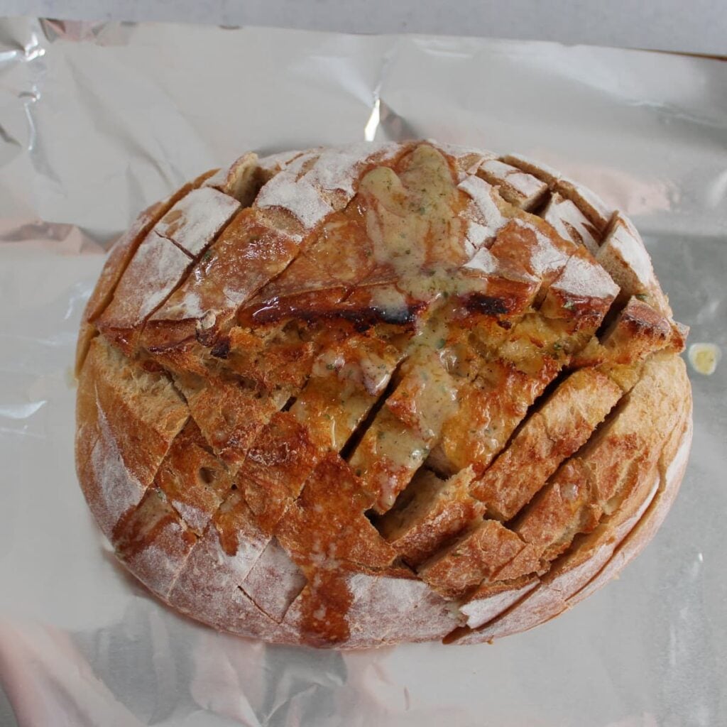 A sourdough loaf sliced and butter ranch mixture added on top on a piece of foil.