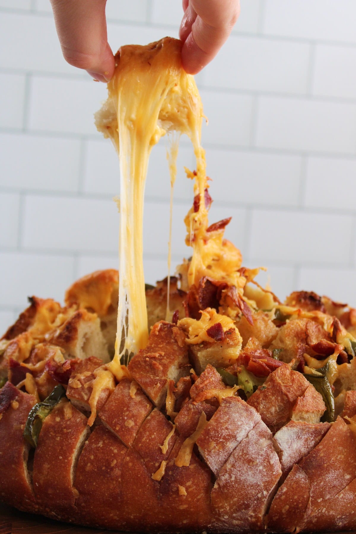 A hand pulling a piece out of the jalapeno cheddar bacon pull apart bread with a cheese pull.