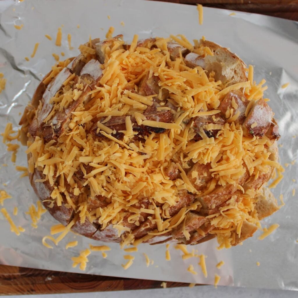A sourdough loaf sliced and filled with ranch, butter and cheddar cheese on a piece of foil.