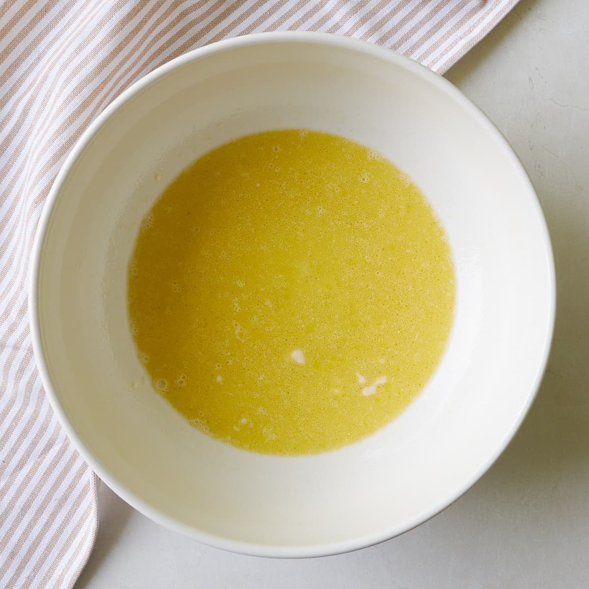 Milk, sourdough discard, oil, and an egg combined in a white bowl for baked sourdough donuts.