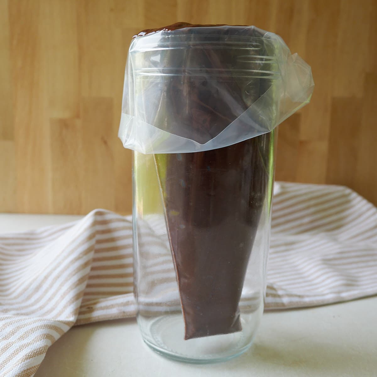 Sourdough chocolate donut batter in a piping bag in a clear cup.