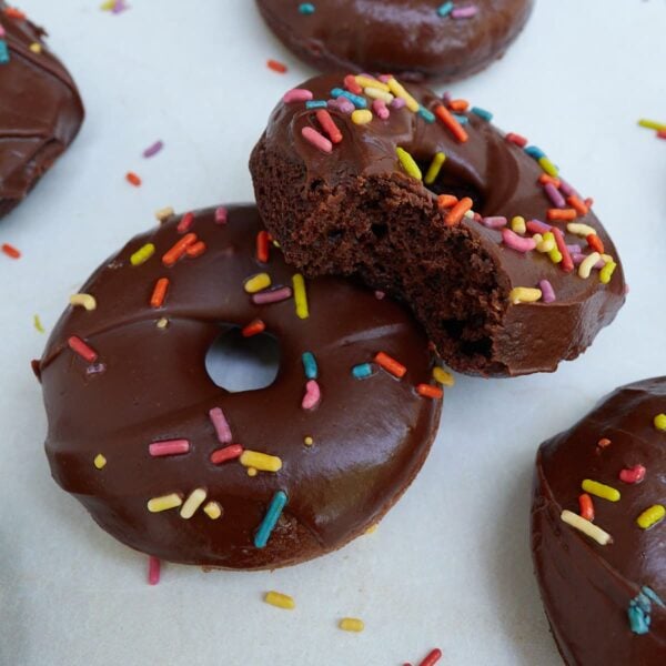 Sourdough chocolate donuts with sprinkles and one has a bite taken out of it.