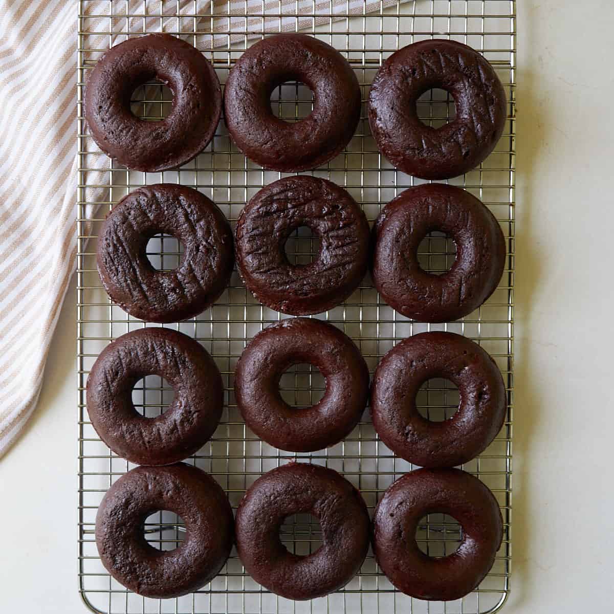 A dozen baked sourdough chocolate donuts cooling on a wire cooling rack.