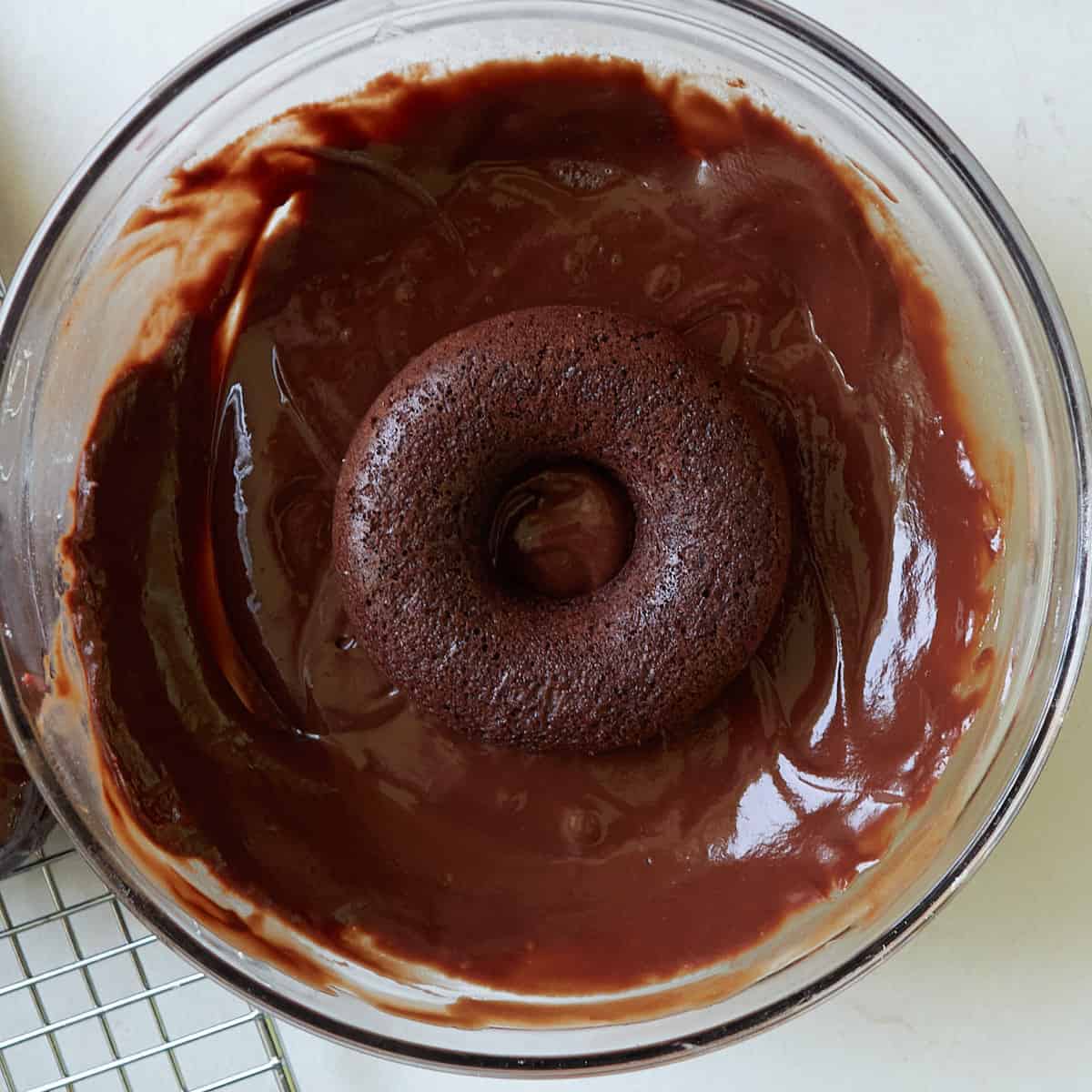 A sourdough chocolate donut dipped in a milk chocolate icing in a glass bowl.