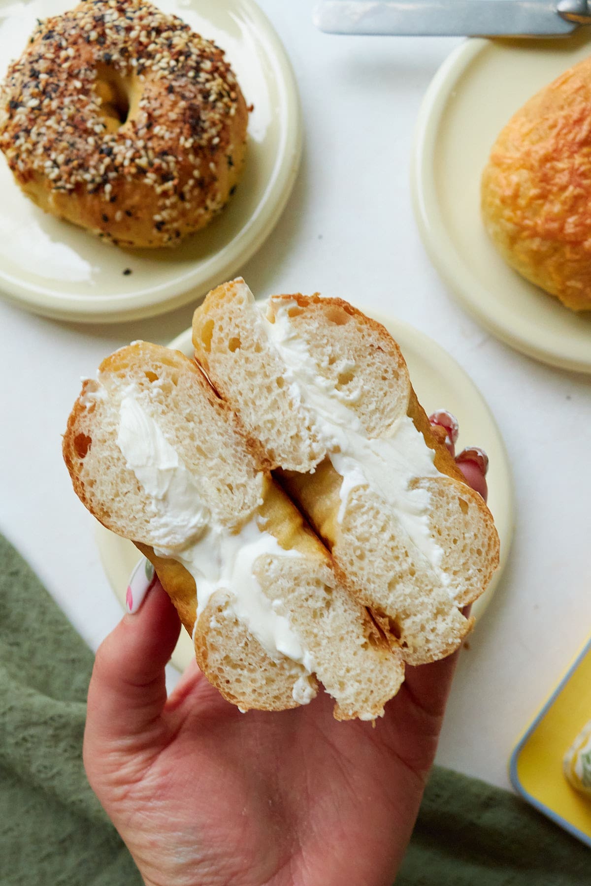 A hand holding a sourdough discard bagel with cream cheese cut in half.