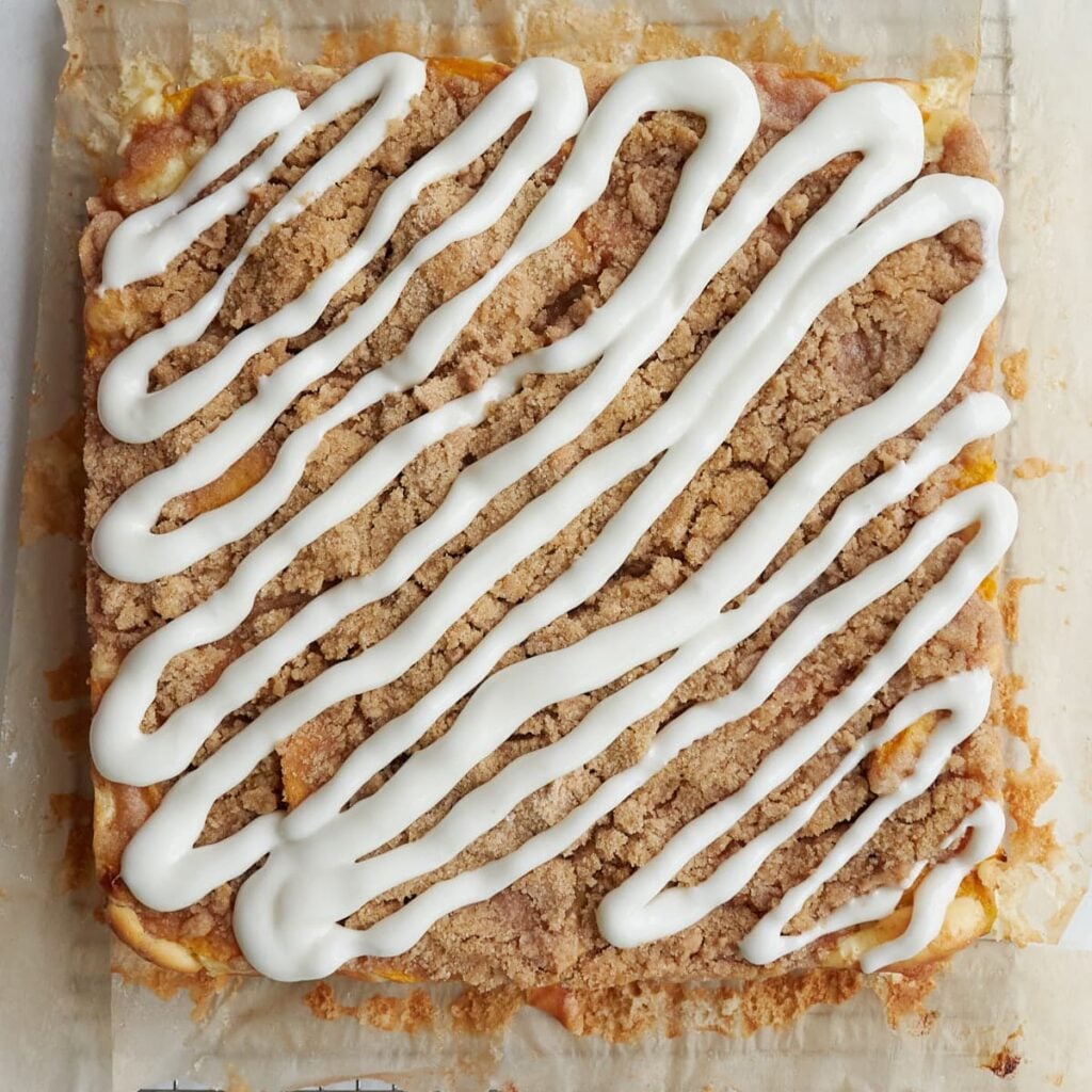 The drizzle added on top of freshly baked Sourdough Peach Crumble Cheesecake Bars.